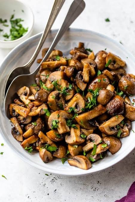 Sautéed garlic mushrooms in a pan, golden and glossy with fresh herbs